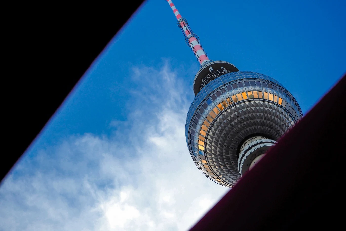 Berlińska Wieża Telewizyjna znajdująca się w berlińskiej dzielnicy Mitte, w pobliżu Alexanderplatz, osiąga wysokości 368 metrów. Fragment Telewizji Berlińskiej z charakterystyczną kulą i anteną na tle niebieskiego nieba, ujęty z nietypowej perspektywy przez ciemne krawędzie.