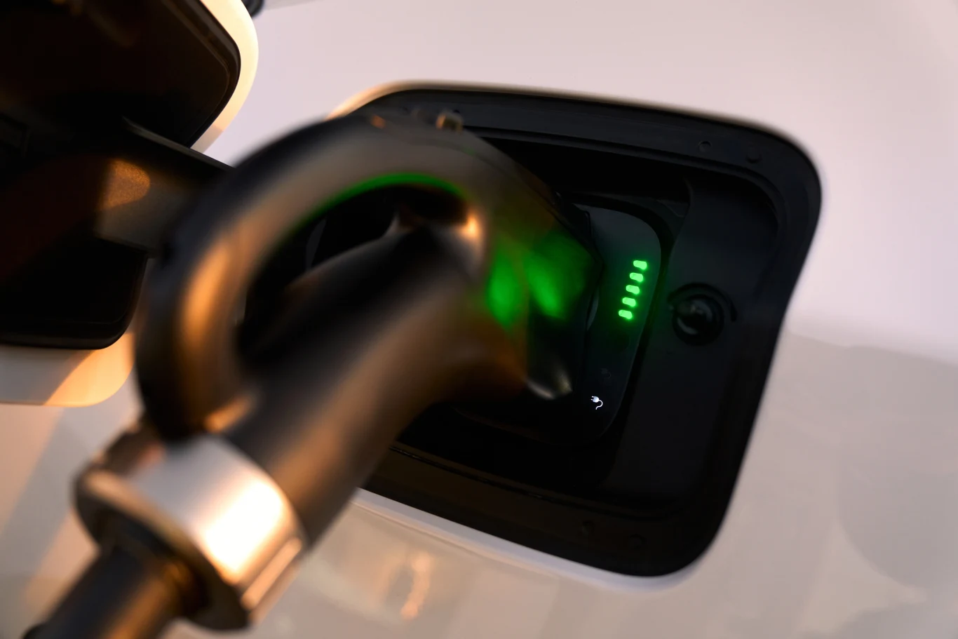 Ujęcie gniazda ładowania samochodu elektrycznego z podłączoną wtyczką oraz podświetleniem wskazującym poziom naładowania.
