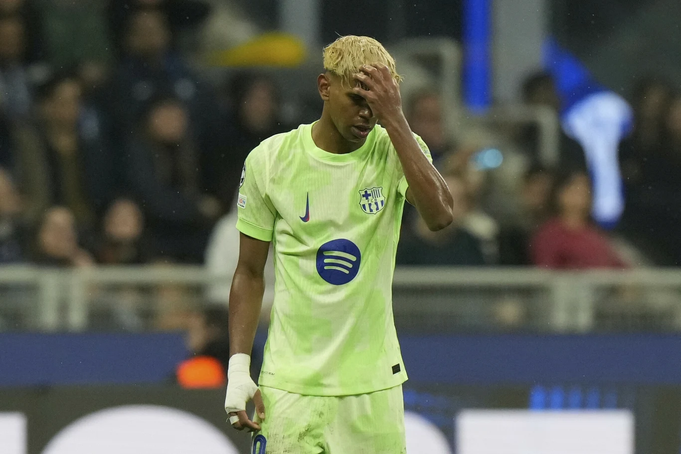 Lamine Yamal Zawodnik piłki nożnej w jasnozielonym stroju z numerem 11 trzyma się za głowę po nieudanej akcji, stojąc na boisku podczas meczu, w tle rozmyta publiczność.