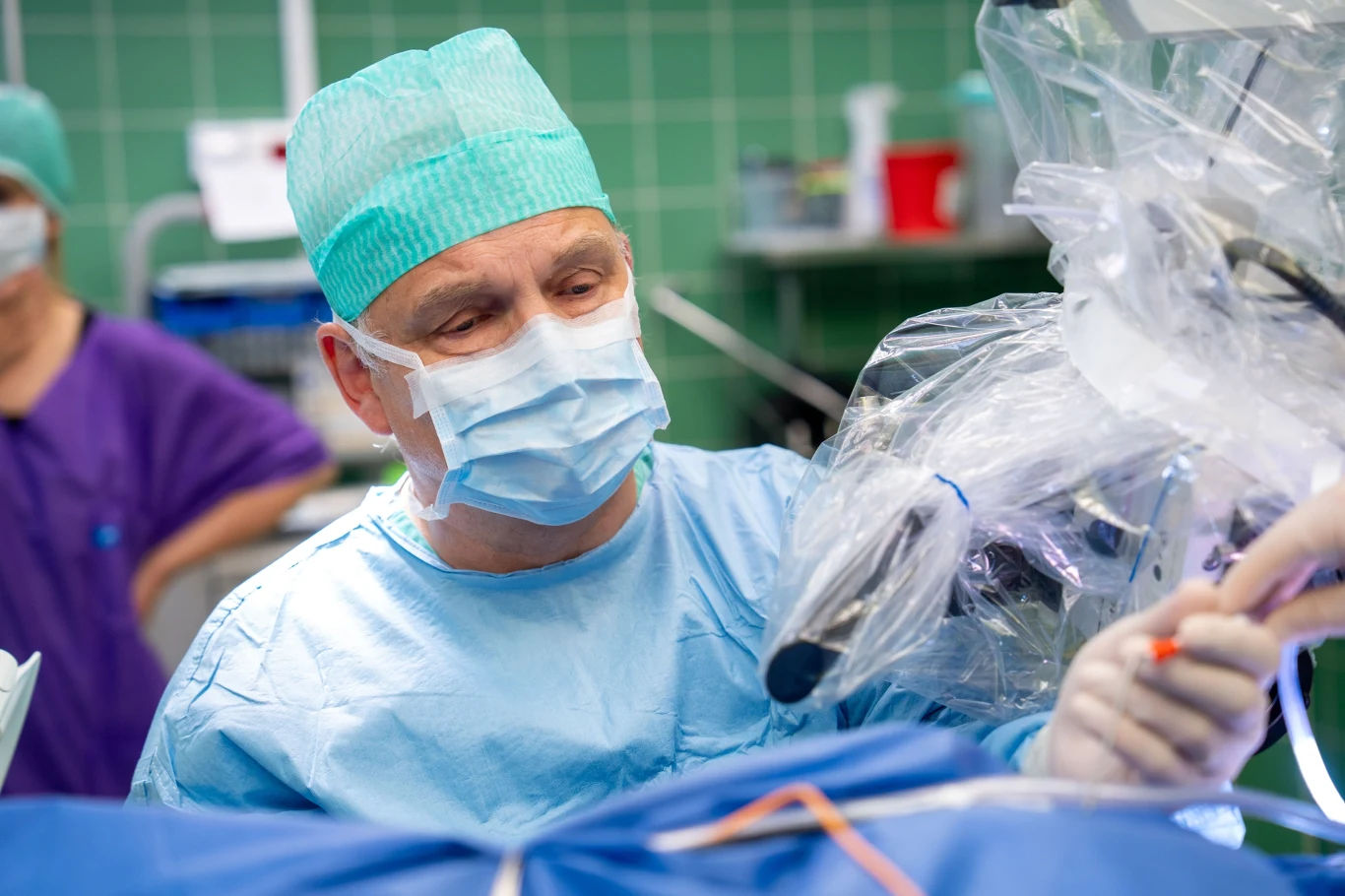 Chirurg w maseczce oraz czepku operacyjnym wykonujący zabieg chirurgiczny przy użyciu nowoczesnego sprzętu medycznego i narzędzi chirurgicznych w sterylnym otoczeniu sali operacyjnej.