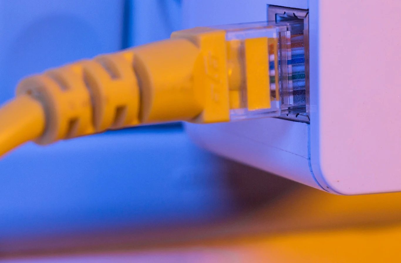 Tak jak twórcom gier udało się wyeliminować loadingi, tak może nadejdą czasy, kiedy wczytywanie treści z ulubionych platform internetowych stanie się niezauważalne Zbliżenie żółtego kabla sieciowego podłączonego do portu ethernetowego w urządzeniu elektronicznym, z niebiesko-pomarańczowym oświetleniem.