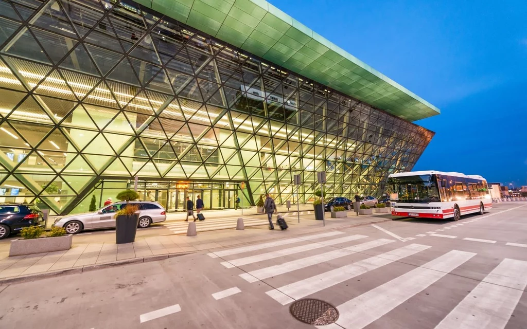 Ekspertka KLM-Air France zdradza kulisy zakupu biletów lotniczych Nowoczesny terminal lotniska z przeszkloną fasadą, przy którym zatrzymał się autobus, widocznych kilka osób z bagażami oraz samochody na postoju przed wejściem.