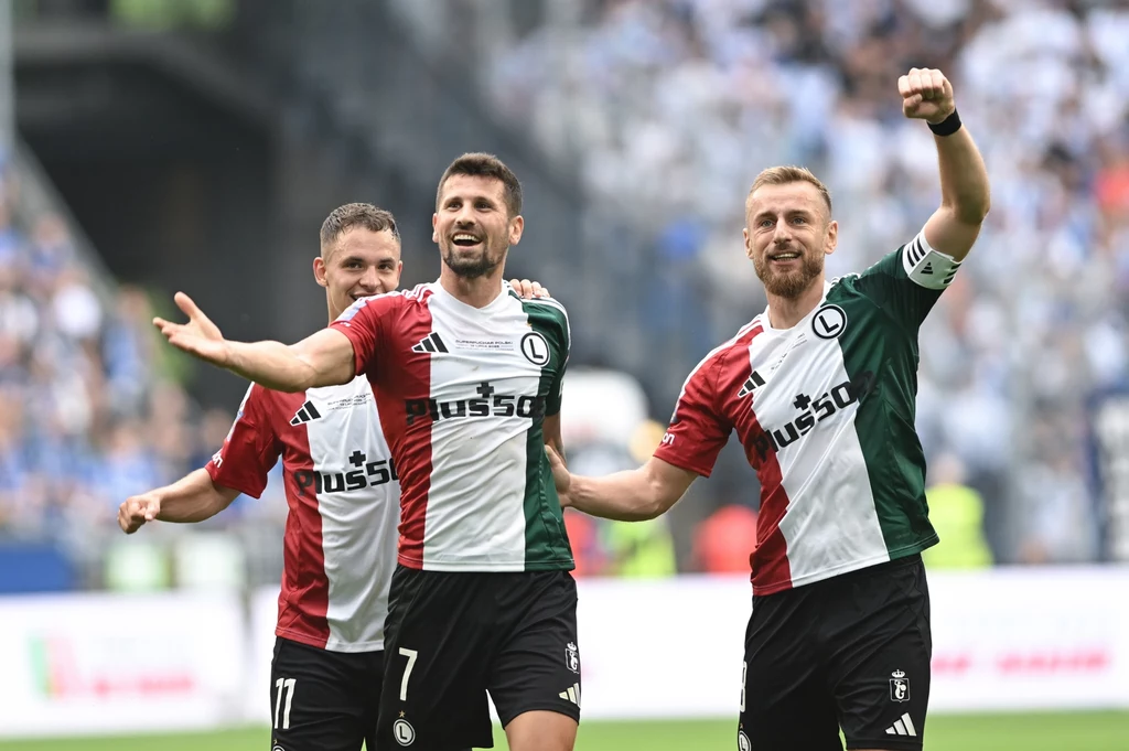 Legia triumfująca w Superpucharze Polski Trzech piłkarzy w pionowych, trójkolorowych koszulkach z logo Legii Warszawa cieszy się ze zdobytej bramki na stadionie, w tle rozmyta widownia oraz inni zawodnicy.