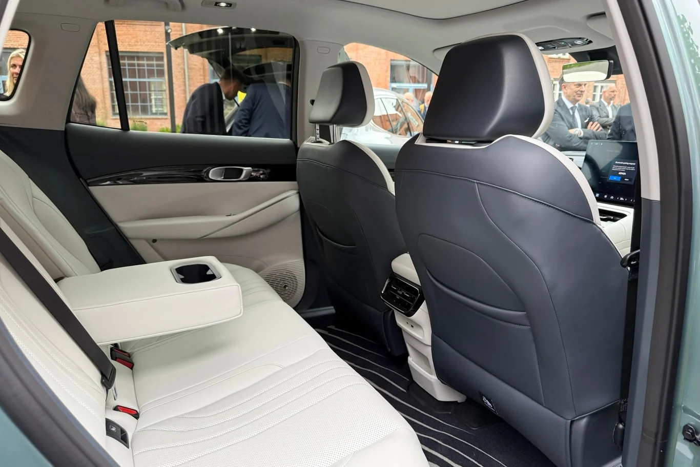 Tylny rząd siedzeń w samochodzie z jasnymi skórzanymi fotelami, podłokietnikiem z miejscem na kubek oraz widokiem na przednie siedzenia i eleganckie wykończenia wnętrza.