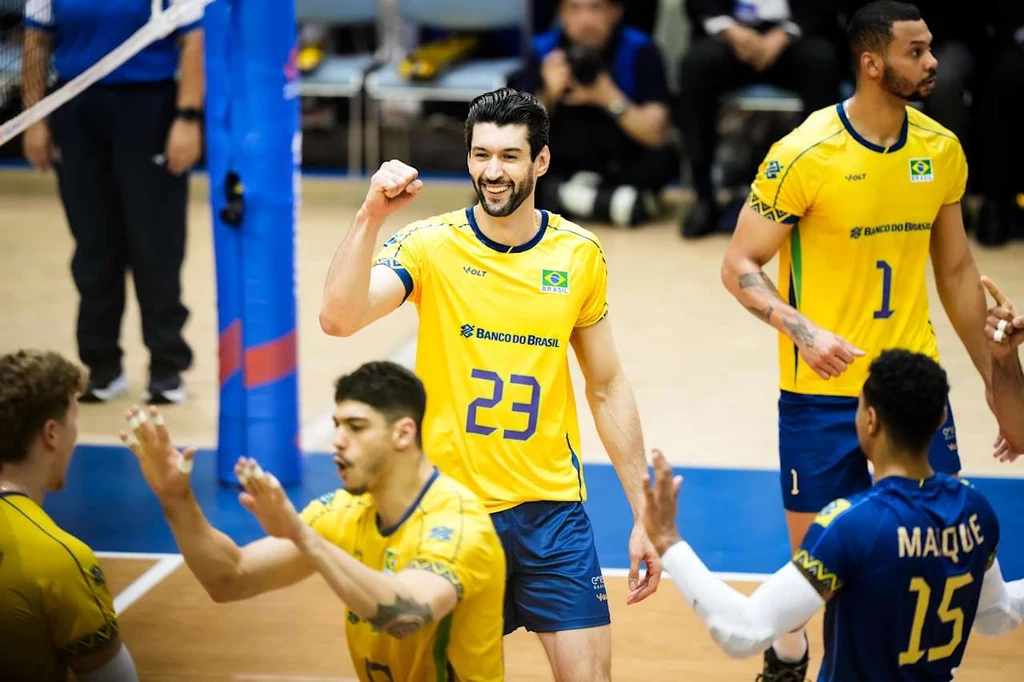 Siatkarze reprezentacji Brazylii Zawodnicy brazylijskiej drużyny siatkówki podczas meczu, centralny gracz z numerem 23 na żółtej koszulce świętuje zdobycie punktu, wokół niego inni zawodnicy oraz fragment siatki.