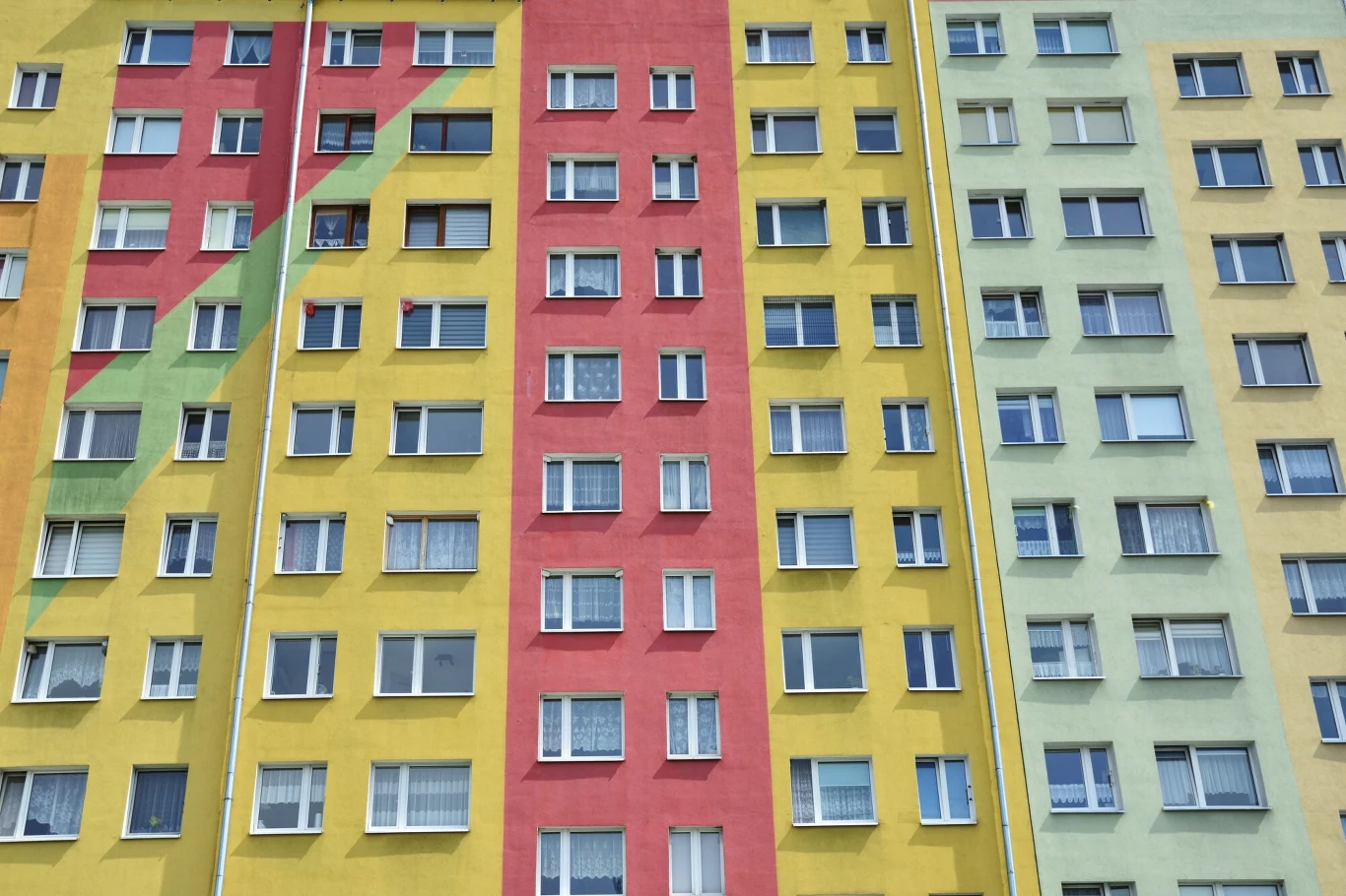 Myślisz, że twój blok zaraz runie? AI ma zaskakującą prognozę Fasada wielopiętrowego bloku mieszkalnego ozdobionego pionowymi pasami w kolorach czerwonym, żółtym i zielonym, z gęsto rozmieszczonymi oknami.