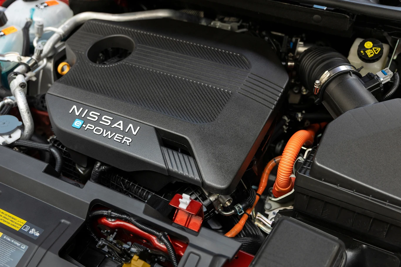 Nowoczesny silnik Nissan e-POWER z widocznymi przewodami i elementami osprzętu, obudowa silnika z wyraźnym oznaczeniem producenta, detale mechaniczne oraz techniczne pod maską samochodu.