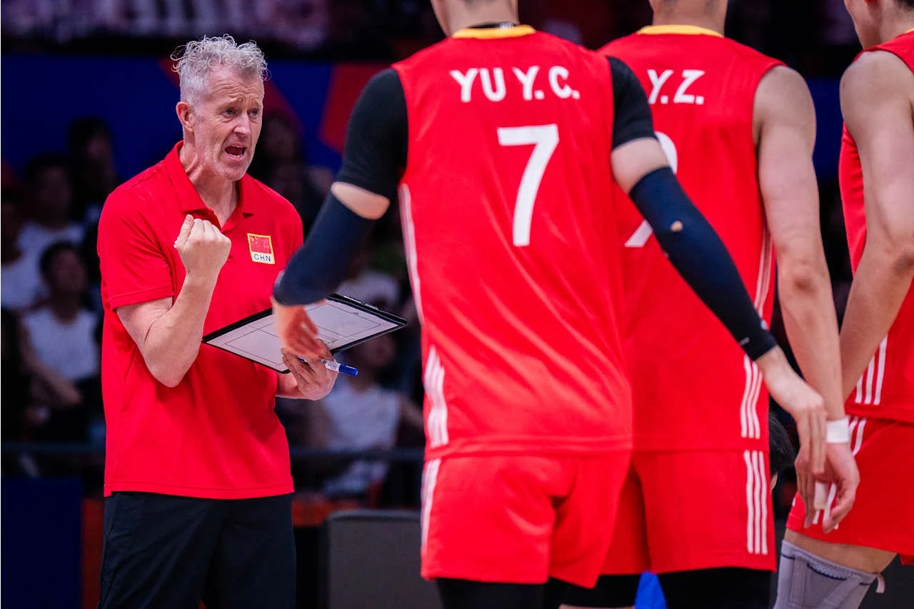Liga Narodów siatkarzy. Vital Heynen prowadzi reprezentację Chin Trener w czerwonej koszulce z uniesioną pięścią, motywuje drużynę siatkówki w czerwonych strojach podczas przerwy meczu.