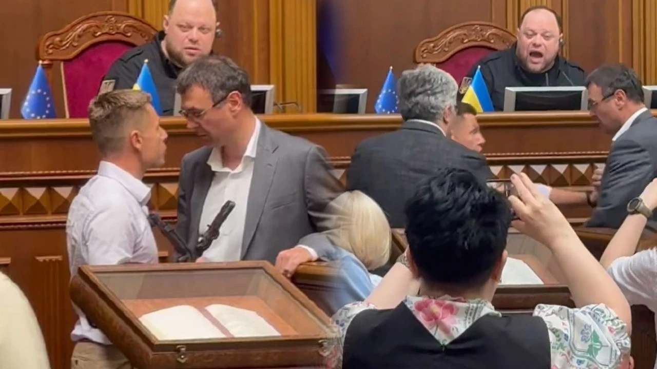 Awantura w ukraińskiej Radzie Najwyższej Grupa polityków rozmawia przy mównicy na tle flag Unii Europejskiej i Ukrainy, w sali posiedzeń parlamentu, kilka osób w garniturach, intensywna dyskusja, jeden z uczestników trzyma mikrofon.
