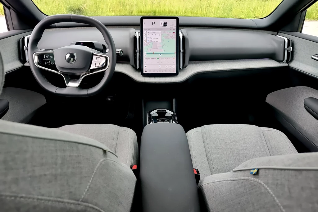 Wnętrze Volvo EX30 śmiało można określić jako ascetyczne Nowoczesne, minimalistyczne wnętrze samochodu elektrycznego z dużym centralnym ekranem dotykowym na konsoli, panoramicznym widokiem na deskę rozdzielczą oraz jasnobrązową tapicerką siedzeń.