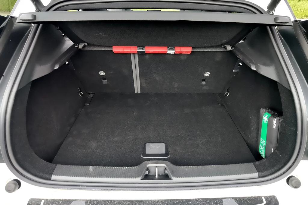 Bagażnik Volvo EX30 ma tylko 318 litrów pojemności Otwarty bagażnik samochodu osobowego z czystą, przestronną przestrzenią załadunkową, na lewym boku umieszczona apteczka, z przodu zamontowane dwa czerwone elementy zabezpieczające.