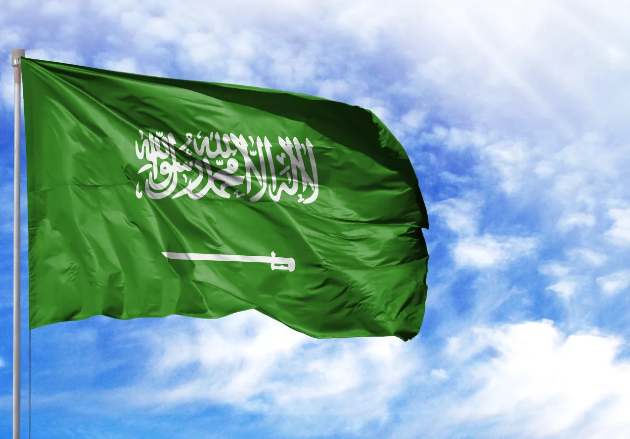 Mistrzostwa w Arabii w cieniu skandalu Zielona flaga z białym arabskim napisem szahady oraz mieczem, powiewająca na tle niebieskiego nieba z chmurami.