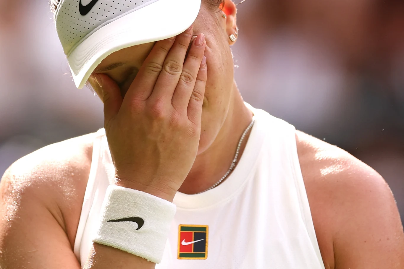 Amanda Anisimova Zawodniczka ubrana w białą sportową koszulkę i czapkę marki Nike zakrywa twarz dłonią, wyrażając emocje takie jak rozczarowanie lub zmęczenie podczas wydarzenia sportowego.