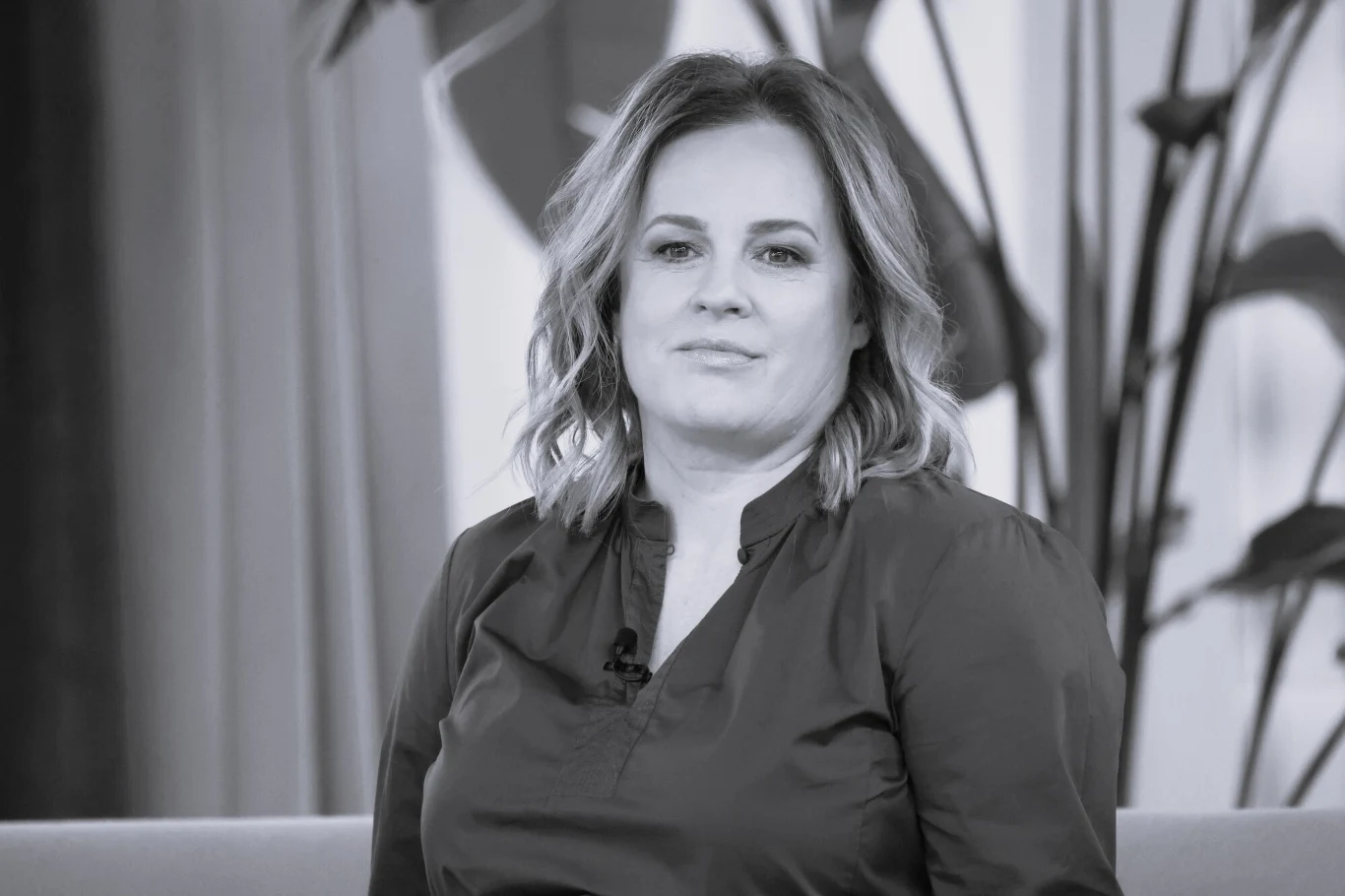 Joanna Kołaczkowska nie żyje Kobieta w średnim wieku z półdługimi jasnymi włosami siedzi na tle roślin w pomieszczeniu i patrzy spokojnie w stronę aparatu.