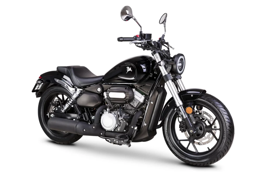 Czarny motocykl typu cruiser z dużym przednim kołem, metalicznymi elementami, pojedynczym siedzeniem oraz okrągłym reflektorem z przodu. Całość utrzymana jest w nowoczesnym, stylowym designie.