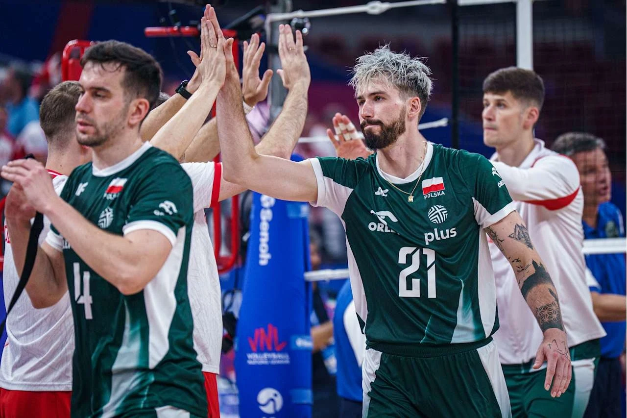 Zawodnicy drużyny siatkarskiej w zielonych strojach podają sobie ręce po zakończonym meczu, na ich twarzach widać zmęczenie i skupienie, w tle inni gracze oraz fragmenty boiska z siatką.