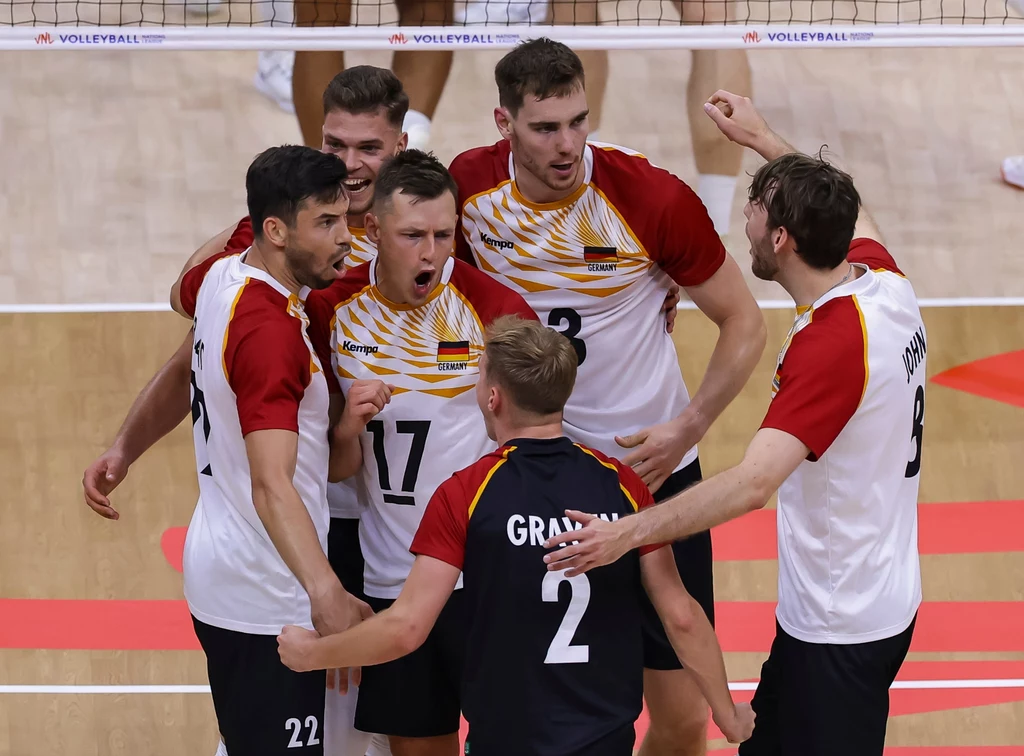 Reprezentacja Niemiec Grupa siatkarzy w sportowych koszulkach stoi blisko siebie na boisku, okazując radość i świętując zdobycie punktu podczas meczu.