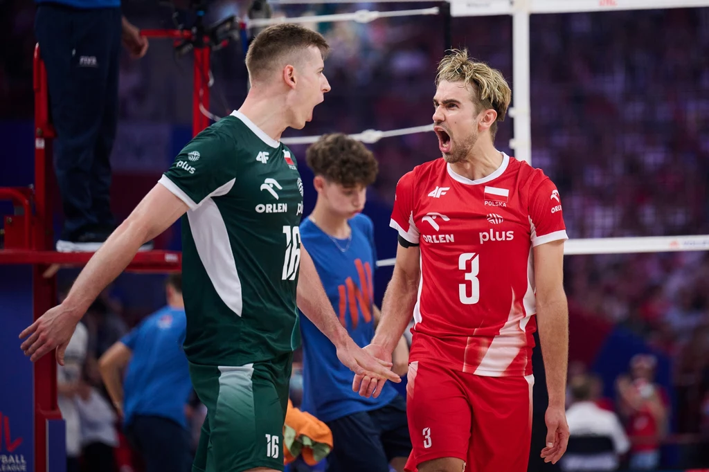 Kamil Semeniuk i Jakub Popiwczak w meczu z Iranem Dwóch siatkarzy w trakcie emocjonującej rywalizacji sportowej, ubrani w profesjonalne stroje reprezentacyjne, jeden w zielonym, drugi w czerwonym, wyrażają silne emocje po udanej akcji, w tle widoczna rozmyta publiczność oraz sędzia.
