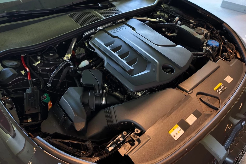 Nowoczesny silnik samochodowy z wyraźnie widocznymi elementami pokrywy silnika oraz detalami technicznymi, pod maską pojazdu marki Audi.