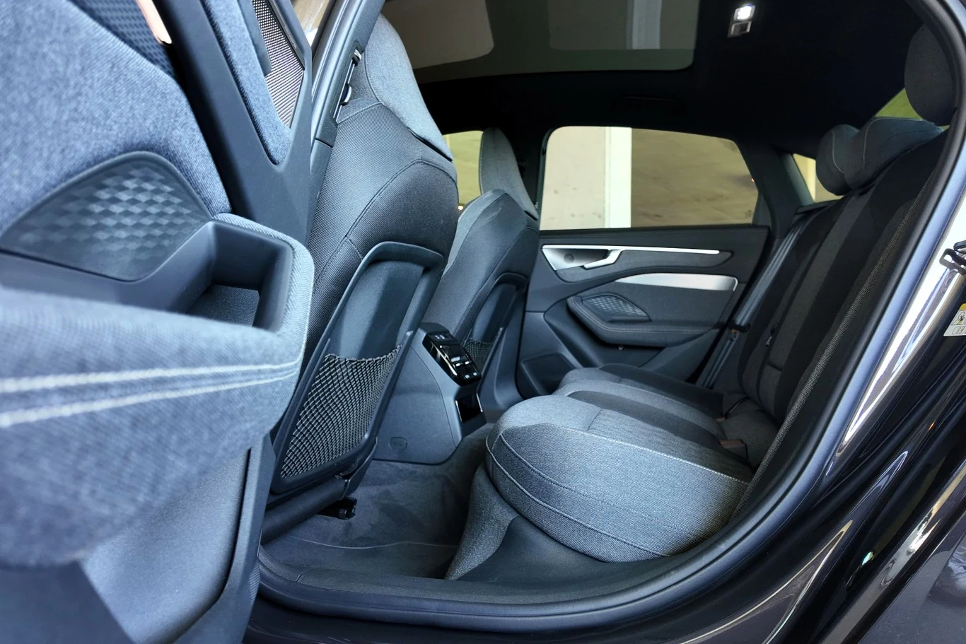 Z tyłu również jest dużo przestrzeni. Pod warunkiem, że nie siadamy na środku. Wówczas komfort będzie zaburzony przez wysoki tunel środkowy. Wnętrze tylnej części samochodu z widocznymi dwoma rzędami siedzeń, ciemną tapicerką, systemem audio oraz dużą ilością miejsca na nogi i nowoczesnymi detalami wykończenia.