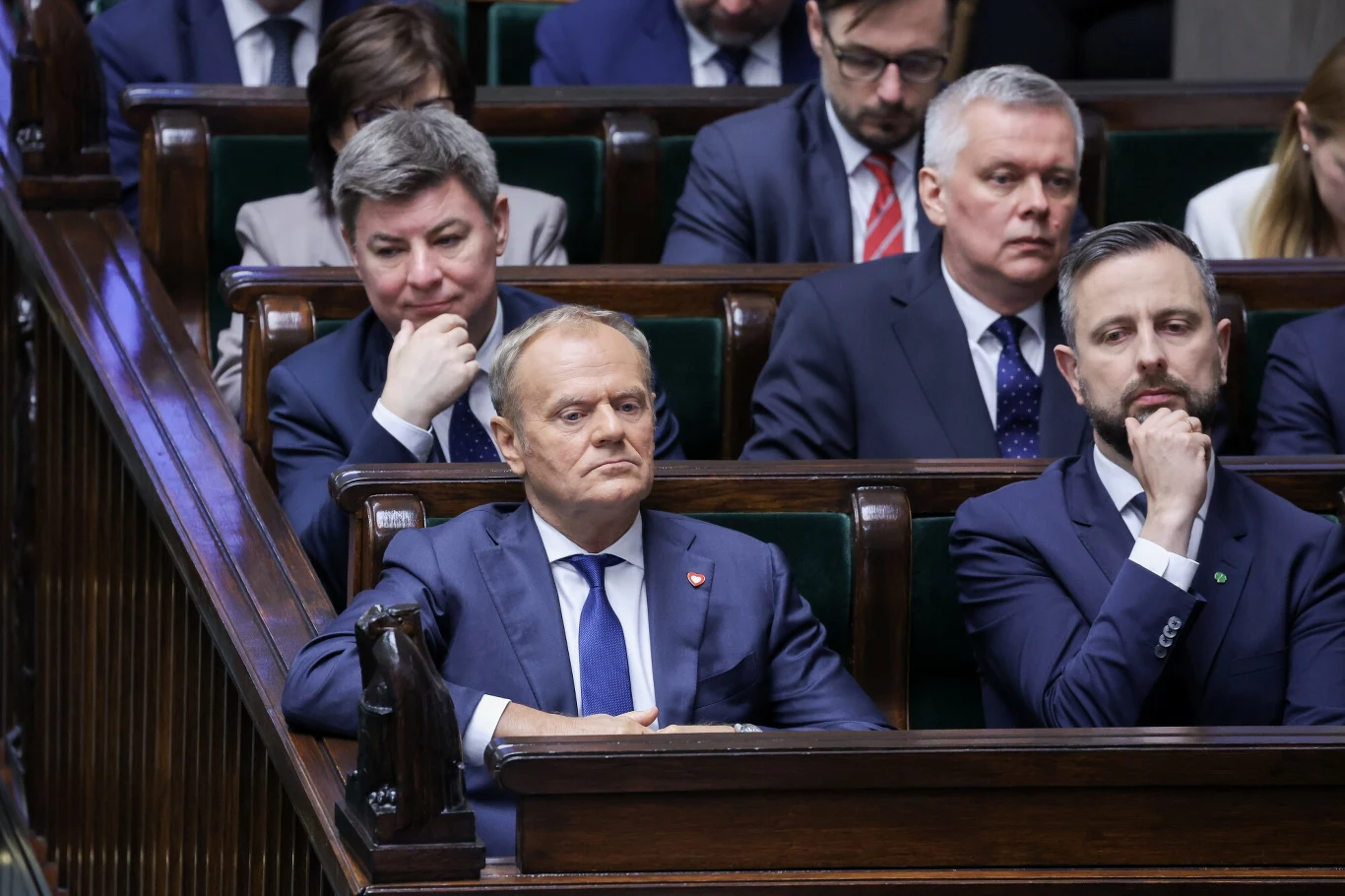 Jak Polacy oceniają pracę rządu Donalda Tuska. Najnowszy sondaż Grupa elegancko ubranych mężczyzn siedzących w ławach parlamentarnych, skupieni i zasłuchani, otoczeni przez innych uczestników posiedzenia.