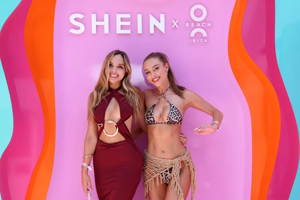SHEIN otwiera sezon letni hucznym pokazem mody na Ibizie Dwie młode kobiety pozują uśmiechnięte na kolorowym tle z logo Shein x O Beach Ibiza, jedna ubrana w efektowną sukienkę, druga w bikini i przewiewną narzutkę, obie prezentują letnią, wakacyjną modę.