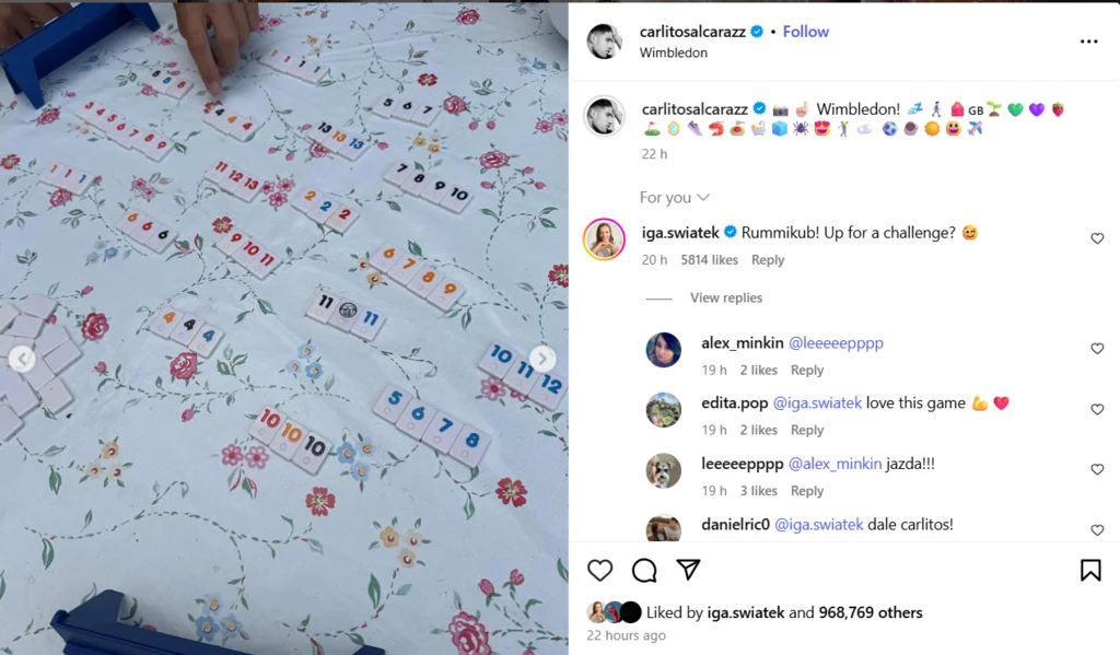 Interakcja Świątek i Alcaraza Rozgrywka gry Rummikub na stole ozdobionym wzorem kwiatowym, kolorowe kostki ułożone w układach, widoczne dłonie graczy przesuwające elementy gry.