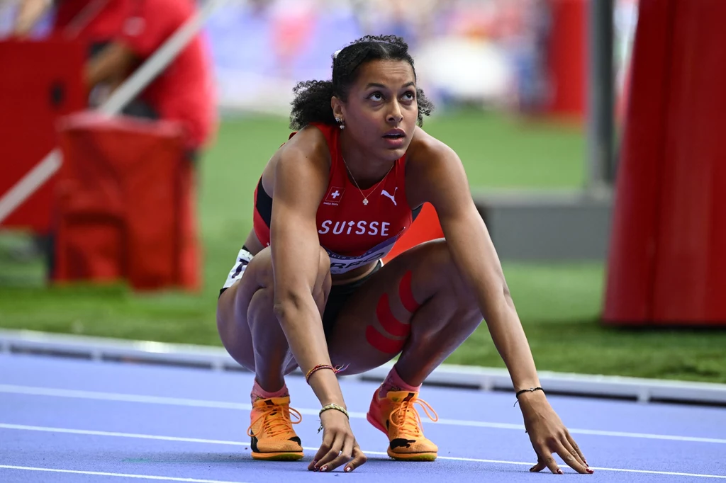Audrey Werro Zawodniczka reprezentująca Szwajcarię w stroju sportowym, przygotowuje się do startu na bieżni lekkoatletycznej, skupiona, z intensywnym wyrazem twarzy, w otoczeniu stadionu.