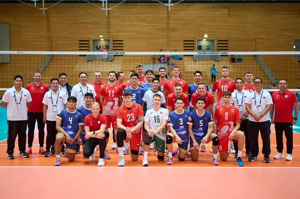 Uniwersjada 2025 Grupa mężczyzn ubranych w sportowe stroje do siatkówki pozuje wspólnie na hali sportowej, część z nich siedzi w pierwszym rzędzie, a reszta stoi z tyłu, za siatką widać trybuny i opustoszałe krzesełka.