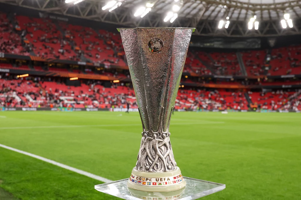 Puchar Ligi Europy UEFA ustawiony na stadionie przed rozpoczęciem meczu, w tle trybuny z kibicami i boisko piłkarskie.