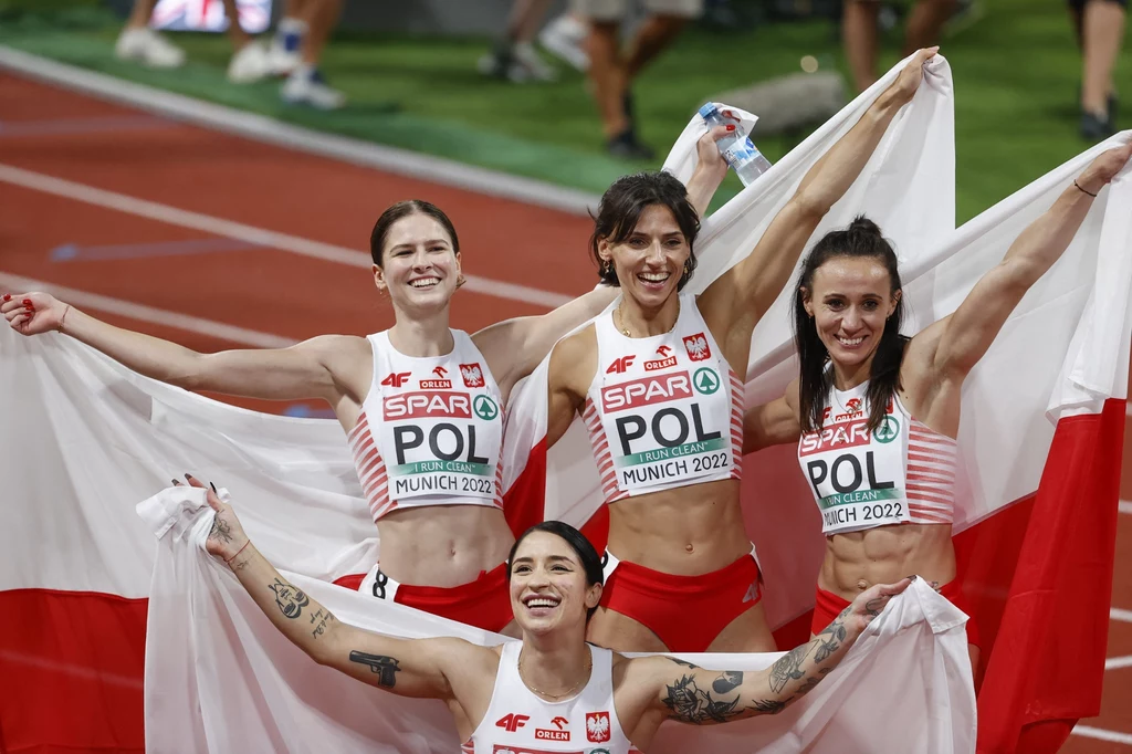Ewa Swoboda, Anna Kiełbasinska, Marika Popowicz-Drapała i Pia Skrzyszowska Cztery polskie lekkoatletki w strojach sportowych trzymają flagi Polski i uśmiechają się radośnie na bieżni stadionu lekkoatletycznego, świętując zwycięstwo podczas zawodów sportowych.