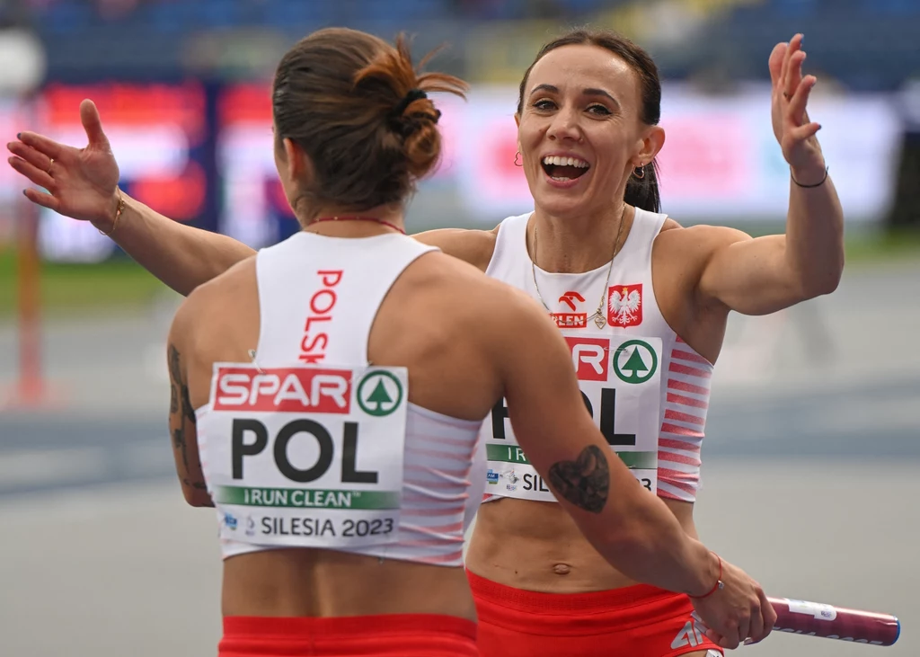 Marika Powowicz-Drapała i Ewa Swoboda Dwie polskie lekkoatletki podczas sztafety na stadionie, jedna przekazuje pałeczkę drugiej, obie ubrane w biało-czerwone stroje z napisami POL i SPAR, jedna z zawodniczek wyraża radość szerokim uśmiechem i rozpostartymi ramionami.