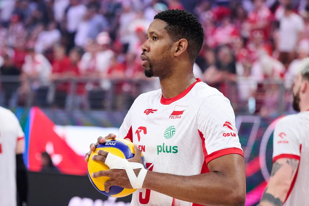 Wilfredo Leon Siatkarz w stroju reprezentacji Polski trzyma piłkę do siatkówki, przygotowując się do zagrywki podczas meczu, w tle widownia i kibice na trybunach.