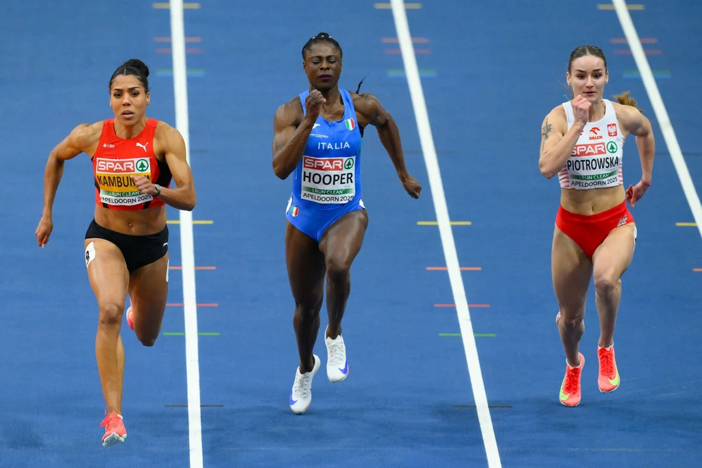 Aleksandra Piotrowska (z prawej) Trzy sportsmenki biegną na bieżni halowej, każda reprezentuje inny kraj; ubrane w stroje sportowe, skupione na osiągnięciu mety, w tle widoczne oznaczenia torów.