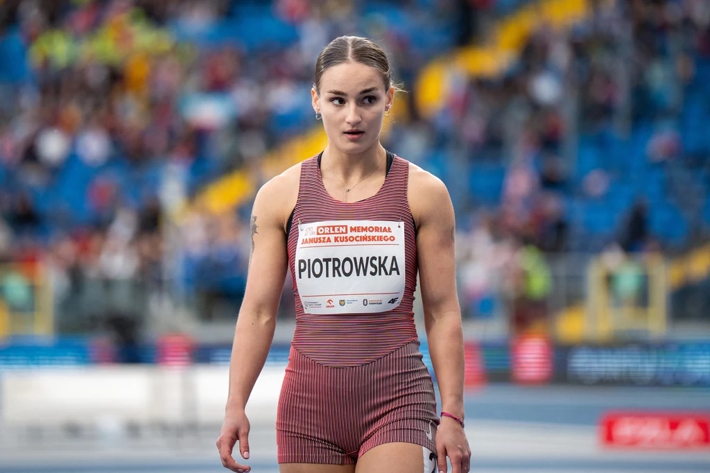 Aleksandra Piotrowska Lekkoatletka w sportowym stroju startowym stoi na stadionie lekkoatletycznym, skupiona i gotowa do rozpoczęcia biegu, w tle rozmyte trybuny z kibicami.