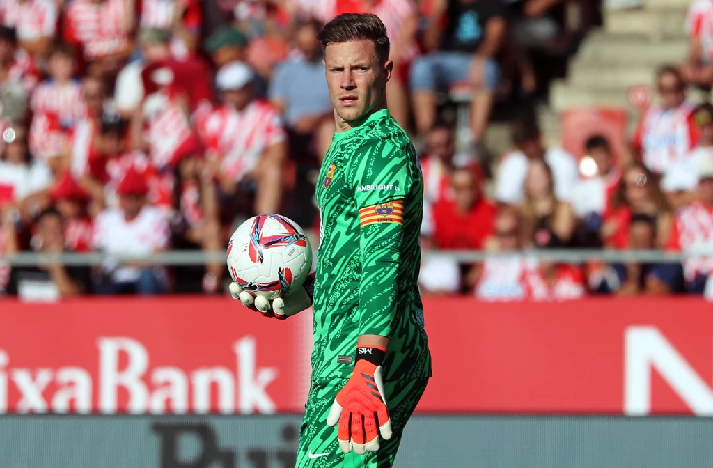Marc-Andre ter Stegen Bramkarz w zielonym stroju meczowym trzyma piłkę na tle stadionu z kibicami ubraną w czerwono-białe barwy