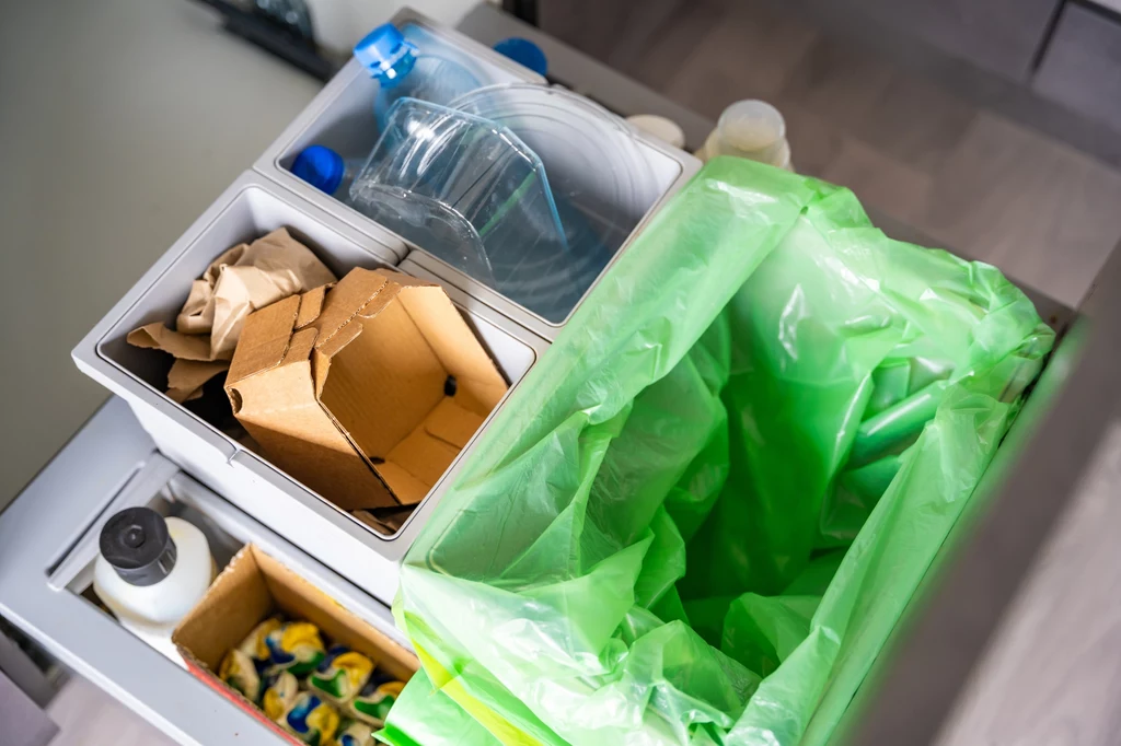 Zużyte ręczniki papierowe nie nadają się do recyklingu, tak więc muszą zostać umieszone w koszu na odpady zmieszane Pojemniki do segregacji śmieci w kuchennej szufladzie, podzielone na miejsce na papier, plastik oraz zwykły odpad, widoczna zielona torba foliowa na śmieci.