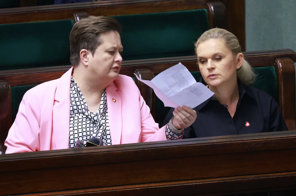 Dwie osoby siedzące obok siebie w ławach sejmowych, w jednej ręce trzymany dokument, który wzbudza ich zainteresowanie i jest analizowany wspólnie.