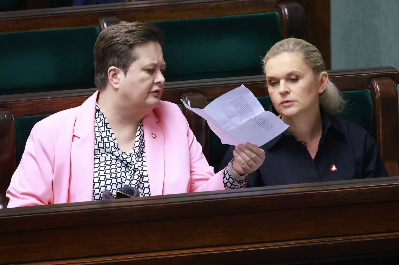 Od lewej: Katarzyna Lubnauer, Barbara Nowacka Dwie osoby siedzące obok siebie w ławach sejmowych, w jednej ręce trzymany dokument, który wzbudza ich zainteresowanie i jest analizowany wspólnie.