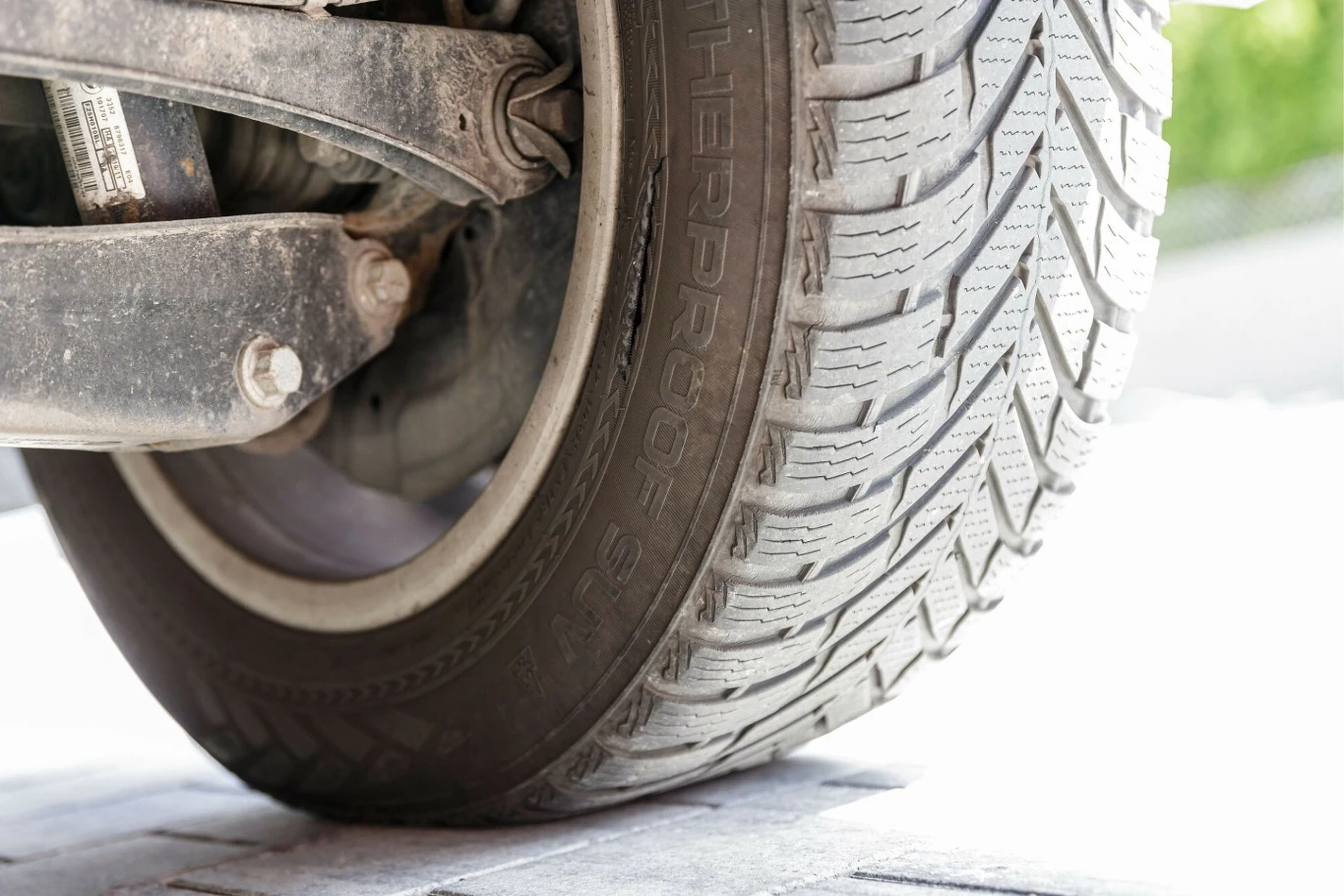 Używanie zimowych opon latem może być nie tylko droższe, ale też niebezpieczne. Koło samochodowe z widoczną oponą oraz fragmentem zawieszenia, szczegóły bieżnika opony i metalowych części konstrukcyjnych.