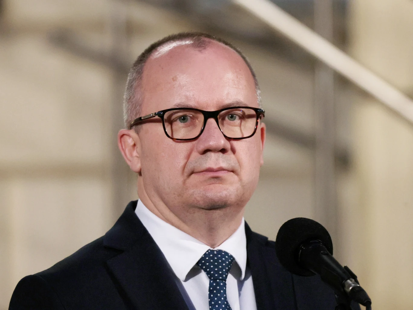 Adam Bodnar skomentował zarzuty dotyczące nominacji generalskiej dla jego brata Mężczyzna w garniturze i okularach stojący przed mikrofonem na lekko rozmytym, jasnym tle, sprawiający wrażenie profesjonalizmu i powagi.