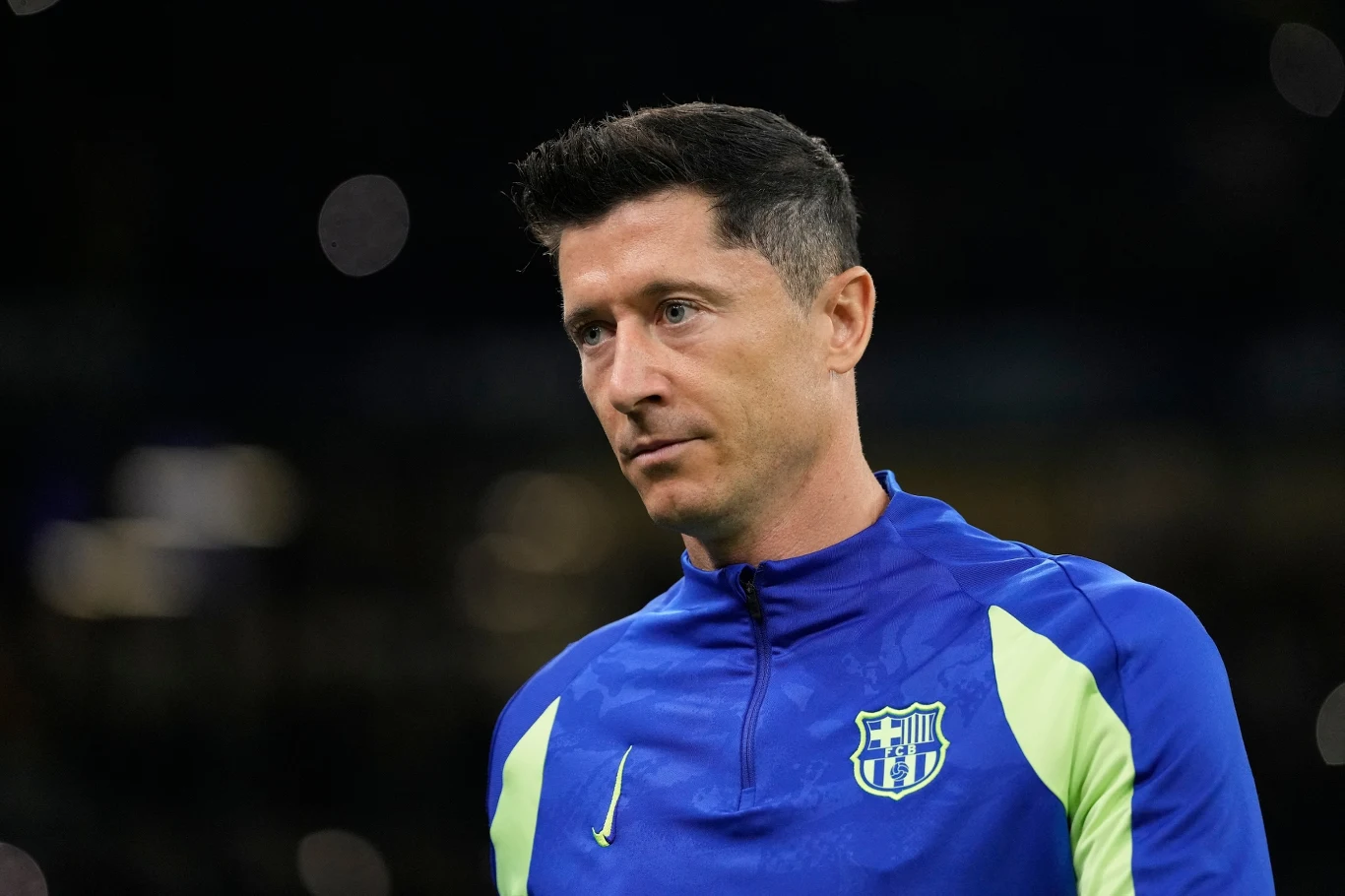 Mężczyzna w sportowej bluzie w barwach klubu FC Barcelona, skoncentrowany na tle rozmytego ciemnego tła