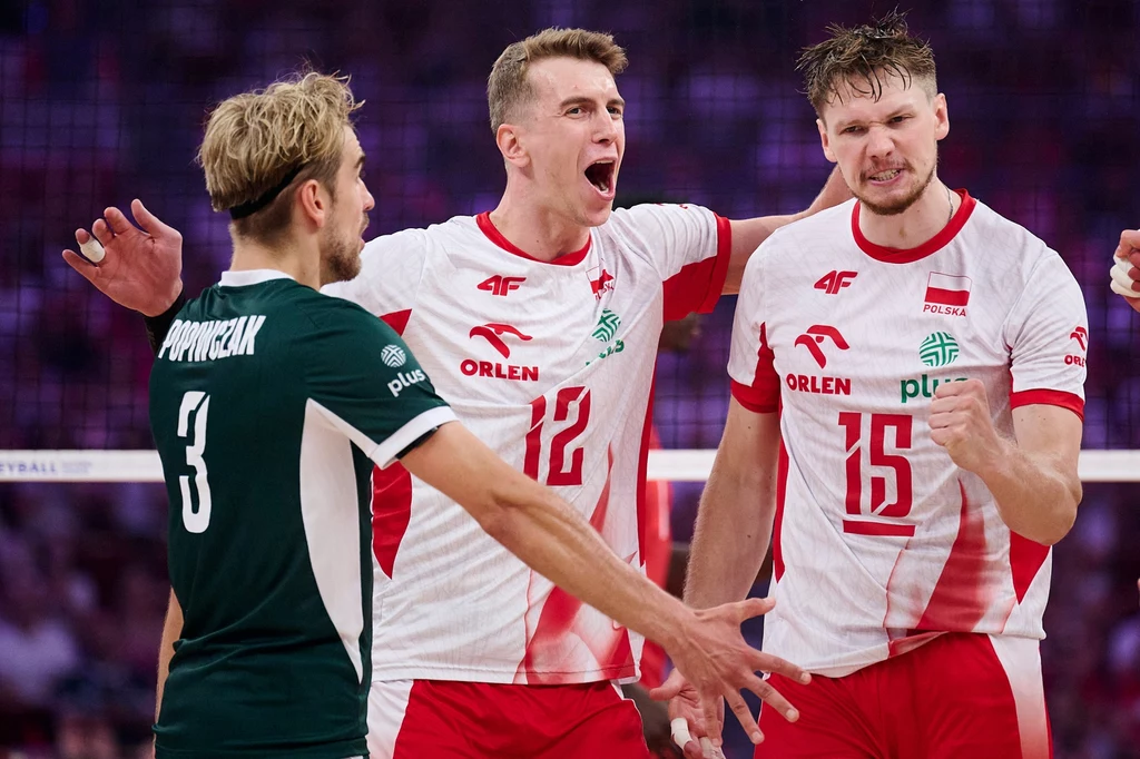 Od lewej: Jakub Popiwczak, Artur Szalpuk i Jakub Kochanowski Trzech siatkarzy podczas sportowej rywalizacji, dwóch ubranych w białe stroje z czerwonymi akcentami świętuje punkt, wyrażając emocje; zawodnik w zielonej koszulce z nazwiskiem na plecach zwrócony do nich plecami.