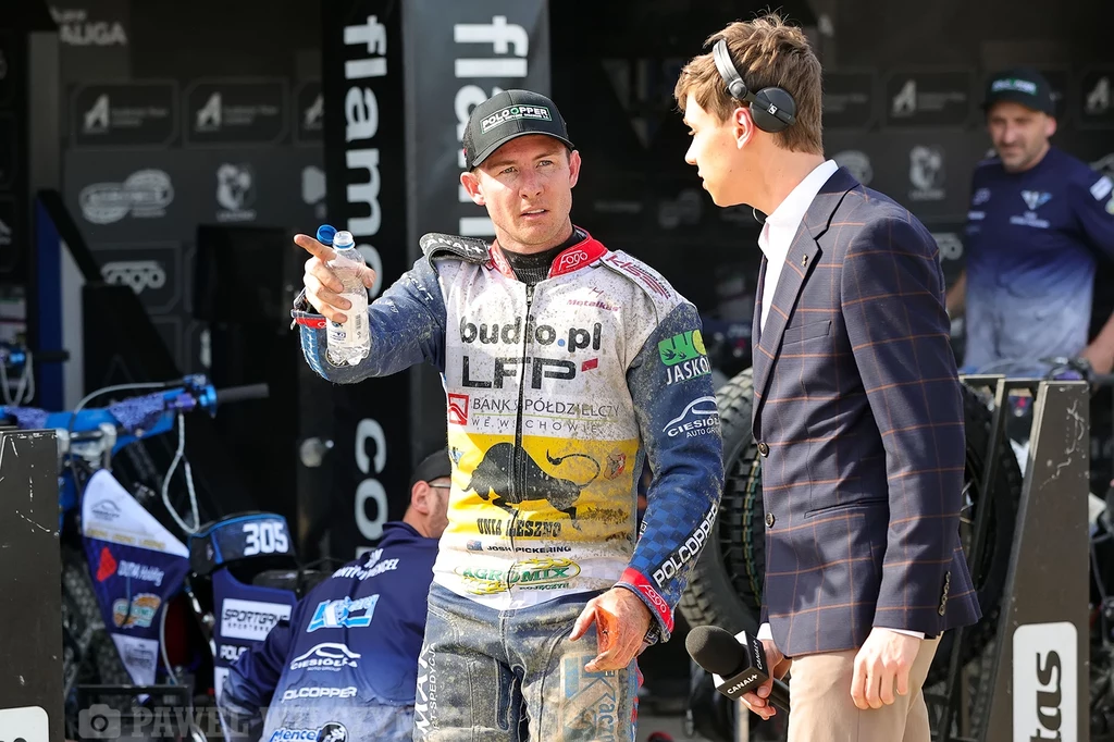 Josh Pickering Żużlowiec w kombinezonie wyścigowym rozmawia z dziennikarzem trzymającym mikrofon, w tle widoczny zespół techniczny i motor żużlowy.