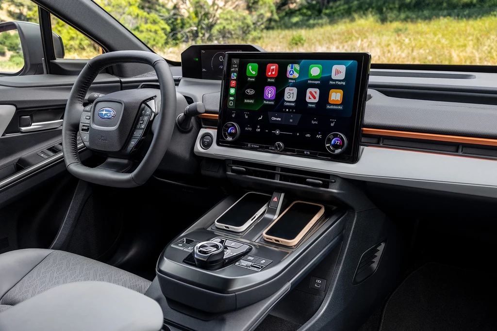 Wnętrze nowoczesnego samochodu Subaru z dużym centralnym ekranem dotykowym pokazującym aplikacje multimedialne, dwa smartfony w konsoli środkowej, kierownica z logiem marki oraz jasne, przestronne wykończenie kokpitu.