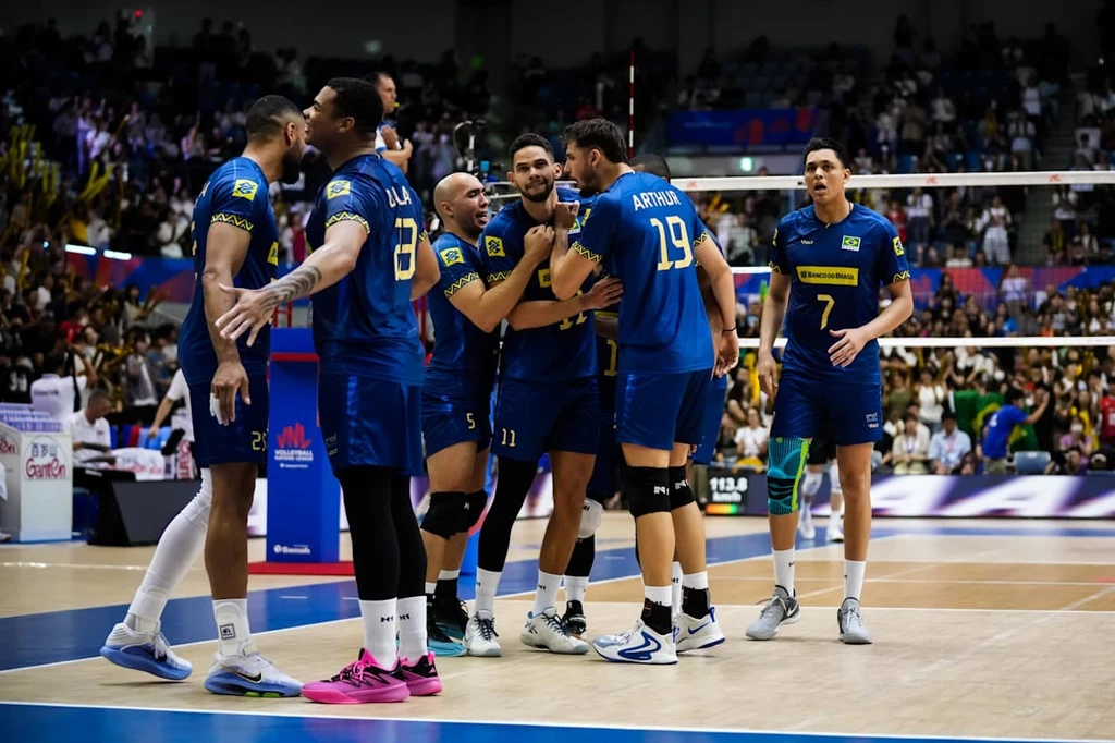 Reprezentacja Brazylii Grupa siatkarzy w niebieskich strojach świętuje punkt na boisku, wokół nich zapełnione trybuny, a w tle widoczna jest siatka i fragment hali sportowej.