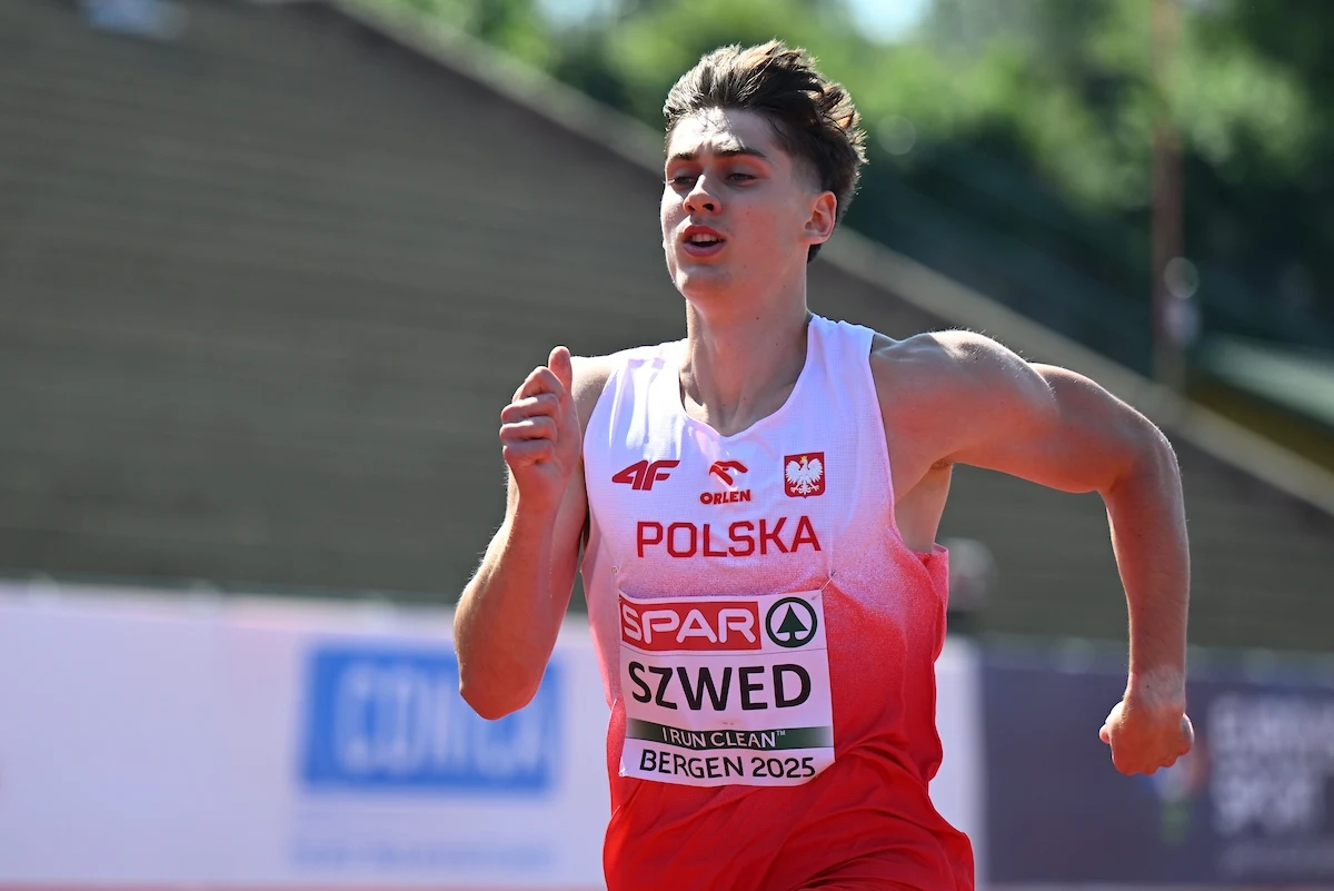 Młody lekkoatleta w stroju reprezentacji Polski biegnie podczas zawodów lekkoatletycznych, z widocznym na koszulce nazwiskiem, nazwą kraju oraz oznaczeniem miasta gospodarza. Skupiona wyraz twarzy, dynamiczny ruch rąk i sylwetka w ruchu wskazują na wys...