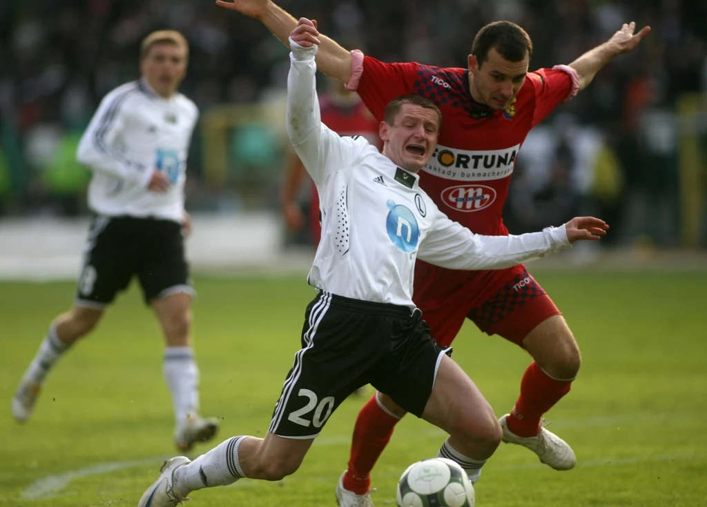 Odra Wodzisław Śląski po raz ostatni w Ekstraklasie grała w sezonie 2009/10 Dwóch piłkarzy walczy o piłkę podczas meczu piłki nożnej, jeden z zawodników upada, drugi próbuje go powstrzymać, w tle widoczni są inni gracze oraz rozmyta publiczność na stadionie.