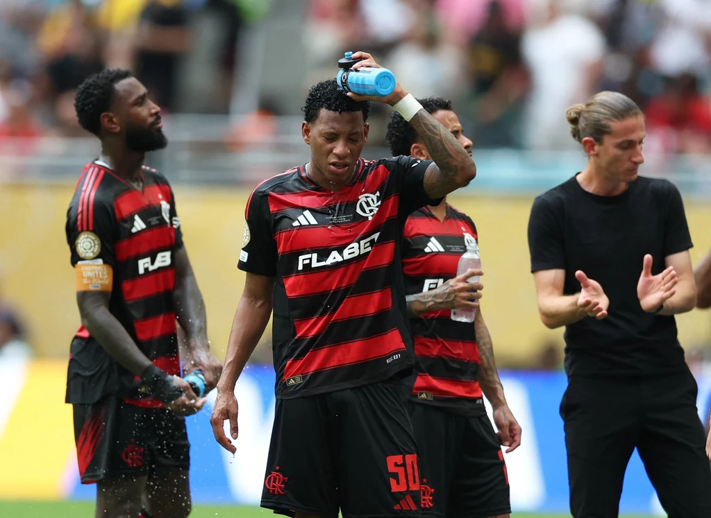 Piłkarze Flamengo chłodzą się podczas meczu z Bayernem Monachium Zawodnicy drużyny piłkarskiej w czerwono-czarnych strojach odpoczywają na boisku, jeden z nich polewa głowę wodą, w tle widoczna publiczność oraz członek sztabu zespołu.