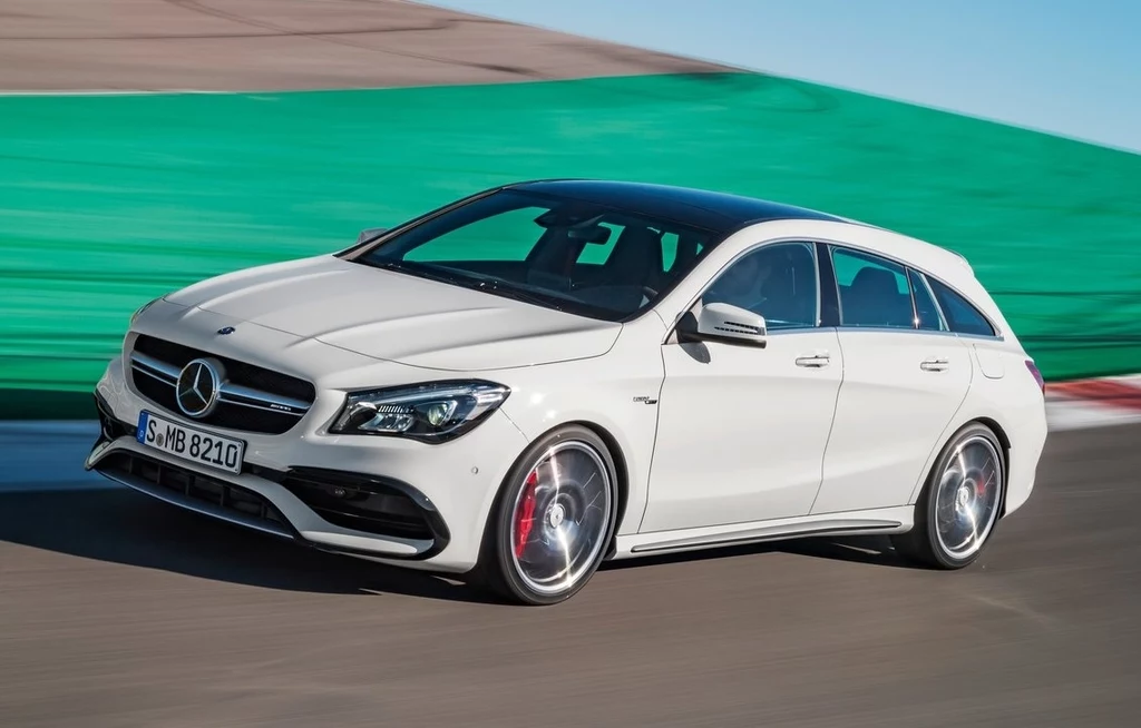 Biały samochód marki Mercedes w wersji kombi jadący po torze, dynamiczna sylwetka auta, widoczne sportowe felgi i czarne elementy dachu, w tle zielona bariera ochronna.